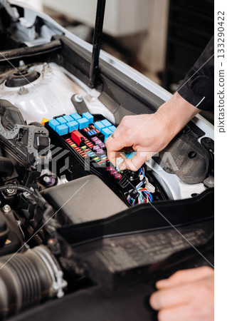 Mechanic replacing car fuse in engine bay fuse box, auto service maintenance close up Mechanic replacing car fuse in engine bay fuse box, auto service maintenance close up 133290422