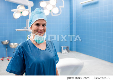 Female surgeon in scrubs standing in operating room beside table under overhead light fixtures 133290609