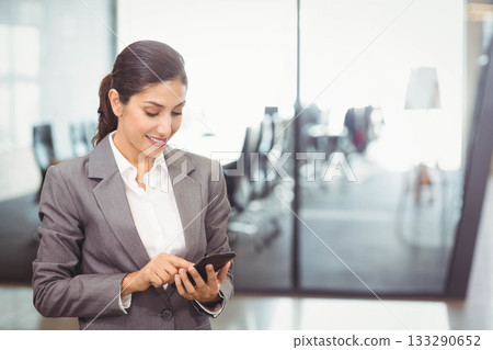 Asian woman wearing gray suit using smartphone in office by glass partition, copy space Asian woman wearing gray suit using smartphone in office by glass partition, copy space 133290652