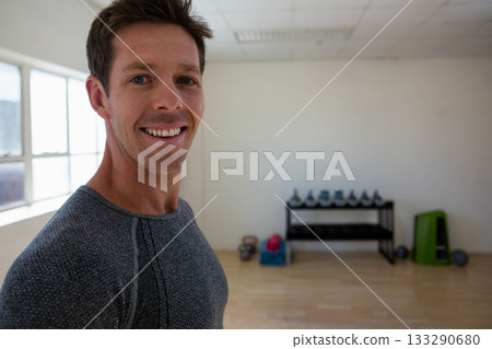 Man standing and smiling by dumbbells, kettlebells and plyometric box in fitness studio, copy space Man standing and smiling by dumbbells, kettlebells and plyometric box in fitness studio, copy space 133290680