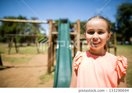 School-age girl standing in front of wooden playset near green slide at public park, copy space 133290694