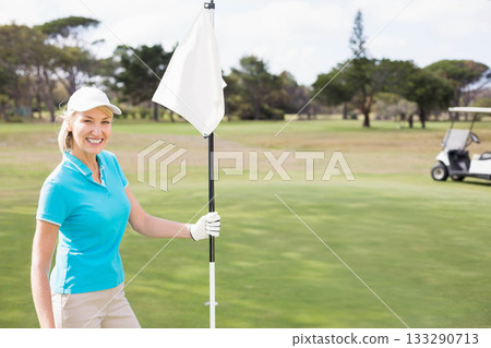 Woman holding white flagstick on putting green, golf hole, golf glove, golf cart, copy space 133290713