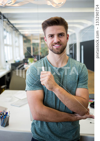 Man standing at desk in open-plan office holding whiteboard marker with computer monitors nearby 133290714