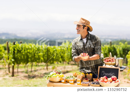 Senior man holding basket of berries at farm stall by vineyard displaying jars, chalkboard sign Senior man holding basket of berries at farm stall by vineyard displaying jars, chalkboard sign 133290732