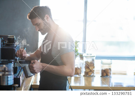 Male barista using milk pitcher steaming milk under espresso machine wand at cafe counter Male barista using milk pitcher steaming milk under espresso machine wand at cafe counter 133290781