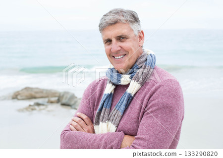 Senior man standing on sandy shore with coastal rocks wearing sweater and striped scarf smiling Senior man standing on sandy shore with coastal rocks wearing sweater and striped scarf smiling 133290820