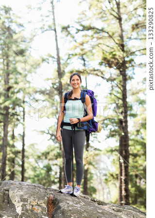Female hiker standing on rock in pine forest gripping poles and carrying purple backpack with pad Female hiker standing on rock in pine forest gripping poles and carrying purple backpack with pad 133290825
