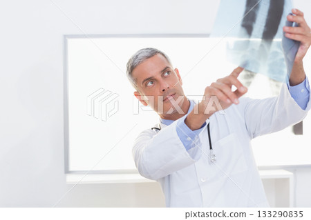 Male doctor in lab coat reading X-ray film on lightbox in clinic with stethoscope, copy space 133290835