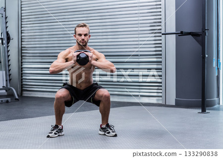 Shirtless man holding kettlebell at chest and squatting on rubber gym floor by pull-up bar Shirtless man holding kettlebell at chest and squatting on rubber gym floor by pull-up bar 133290838