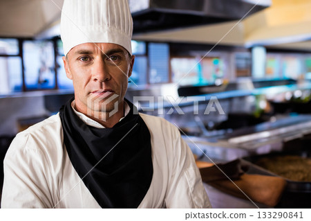 Male chef standing in restaurant kitchen wearing chef's toque and coat under ventilation hood 133290841