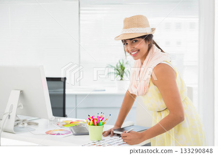 Woman in twenties leaning over office desk wearing straw fedora hat reviewing color swatches Woman in twenties leaning over office desk wearing straw fedora hat reviewing color swatches 133290848