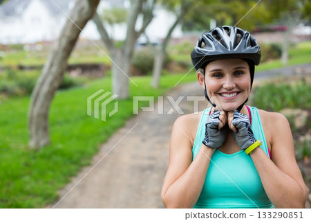 Woman in her twenties fastening helmet strap on park trail, cycling gloves and tracker, copy space 133290851