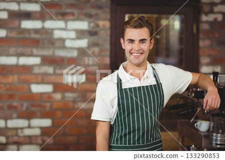 Male barista at cafe leaning on counter by espresso machine with cups, portafilters, copy space 133290853