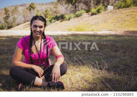 woman in her twenties sitting crosslegged in meadow wearing sweatband holding whistle near sneakers woman in her twenties sitting crosslegged in meadow wearing sweatband holding whistle near sneakers 133290865