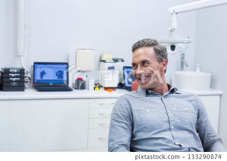 Middle aged man sitting in operatory chair at dental clinic with laptops, overhead lamp, copy space Middle aged man sitting in operatory chair at dental clinic with laptops, overhead lamp, copy space 133290874