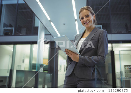 Businesswoman in suit holding tablet, looking at camera in office with glass partitions, copy space Businesswoman in suit holding tablet, looking at camera in office with glass partitions, copy space 133290875