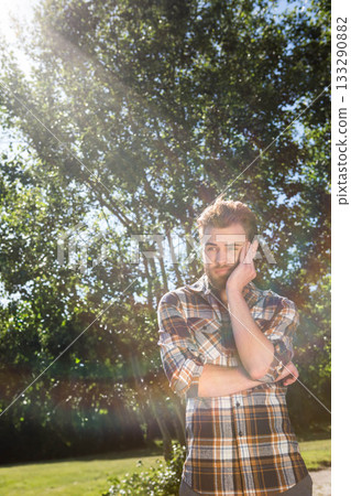 Bearded man wearing plaid shirt leaning head crossing arms in park clearing lens flare, copy space Bearded man wearing plaid shirt leaning head crossing arms in park clearing lens flare, copy space 133290882