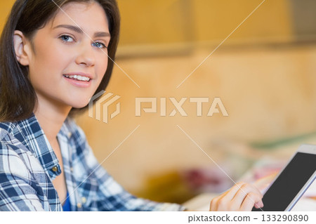Woman wearing plaid shirt holding tablet at wooden table in seating area, copy space 133290890