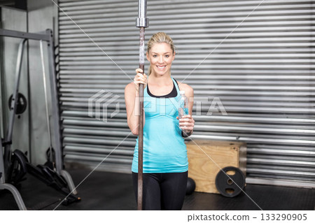 Woman holding barbell pole and water bottle in gym with cable machine, plyometric box, weight plate Woman holding barbell pole and water bottle in gym with cable machine, plyometric box, weight plate 133290905
