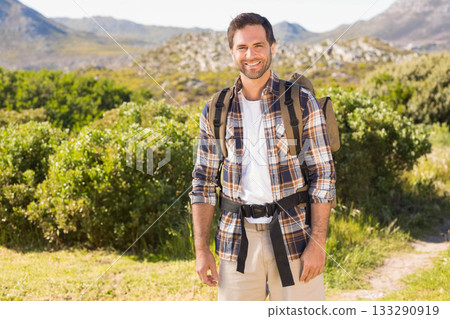 Smiling mid adult man hiking narrow dirt trail with olive-green backpack among distant mountains Smiling mid adult man hiking narrow dirt trail with olive-green backpack among distant mountains 133290919