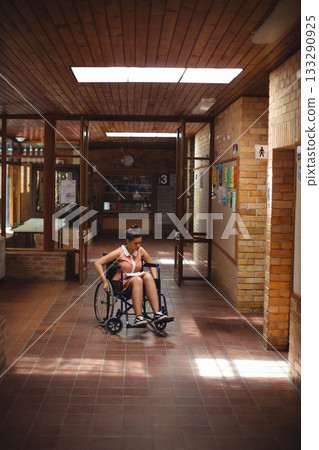 African American teenage student reading notes in notebook in wheelchair in brick-walled hallway 133290925