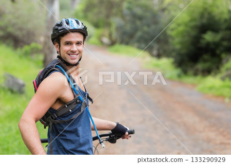 Man smiling while holding bike handlebar on forest trail wearing helmet hydration pack, copy space Man smiling while holding bike handlebar on forest trail wearing helmet hydration pack, copy space 133290929