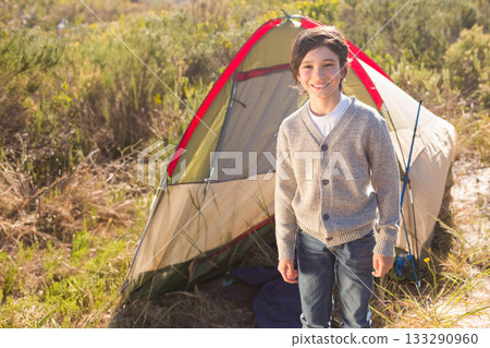 Boy standing and smiling in front of two-person tent at campsite with ground sheet, copy space Boy standing and smiling in front of two-person tent at campsite with ground sheet, copy space 133290960