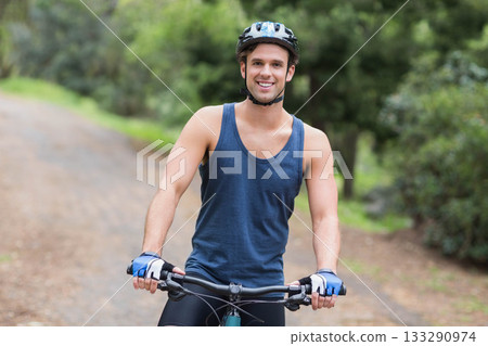 Man riding bicycle wearing helmet and fingerless gloves along gravel trail through dense woods Man riding bicycle wearing helmet and fingerless gloves along gravel trail through dense woods 133290974