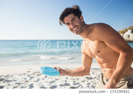 Man in 30s holding blue frisbee disc wearing swim trunks on sandy beach, copy space Man in 30s holding blue frisbee disc wearing swim trunks on sandy beach, copy space 133290981