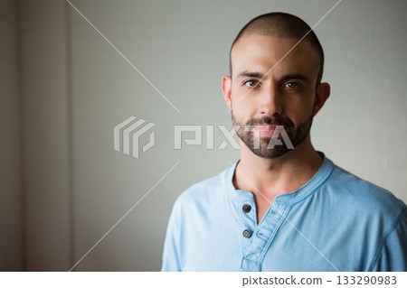 Man standing against smooth painted wall in studio wearing light blue henley shirt, copy space 133290983