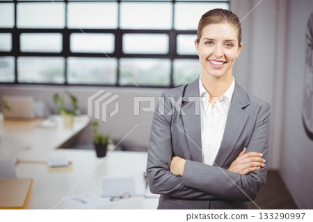 Businesswoman standing with arms crossed by desk with laptop, documents and plants, copy space Businesswoman standing with arms crossed by desk with laptop, documents and plants, copy space 133290997