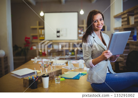 Female professional in blazer holding tablet sitting on table in office with coffee cup, copy space 133291002