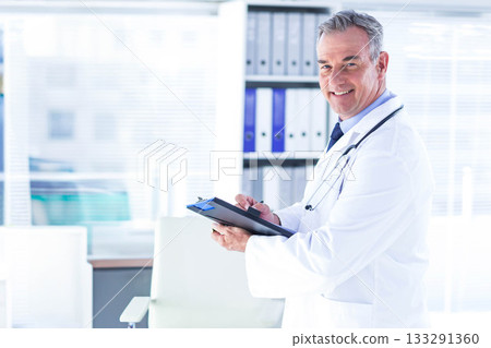 Male doctor writing clipboard with pen in lab coat stethoscope at clinic by shelving, copy space Male doctor writing clipboard with pen in lab coat stethoscope at clinic by shelving, copy space 133291360