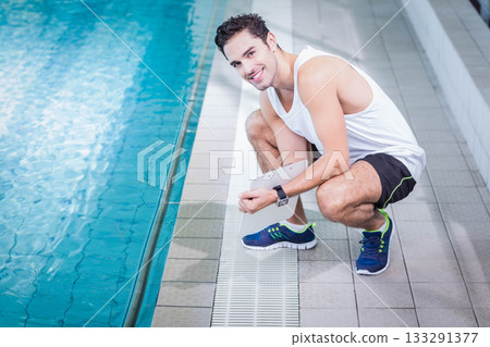 Man crouching at swimming pool deck holding tablet and checking smartwatch display, copy space Man crouching at swimming pool deck holding tablet and checking smartwatch display, copy space 133291377