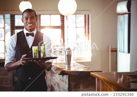 African American man in formal attire serving cocktails on black tray at rustic bar, copy space 133291380