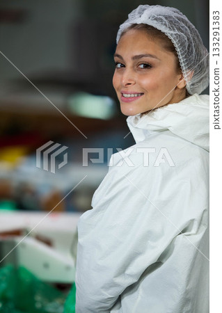Female technician monitoring conveyor in facility wearing hair net and coverall, copy space 133291383