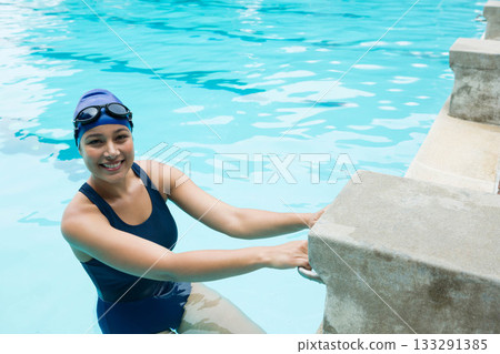 Asian woman holding concrete pool edge in outdoor pool with swim cap and goggles, copy space 133291385