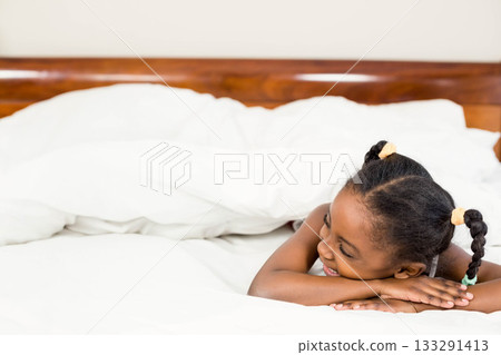 African American child lying on bed smiling amid white pillows and duvet in bedroom, copy space African American child lying on bed smiling amid white pillows and duvet in bedroom, copy space 133291413