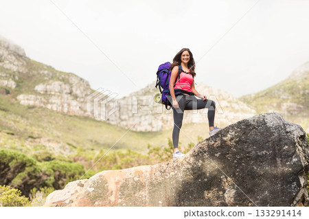 Female hiker standing on boulder at mountain trail with purple backpack and rolled mat, copy space 133291414