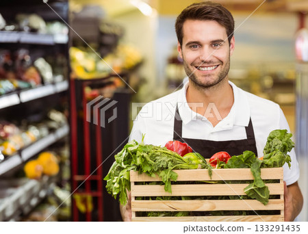 Man holding wooden crate with red and green peppers, leafy greens and herbs in produce section Man holding wooden crate with red and green peppers, leafy greens and herbs in produce section 133291435