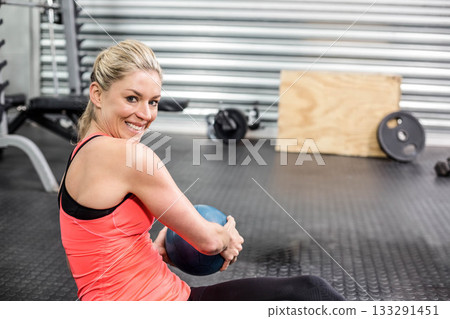 Woman wearing coral tank top and black leggings holding blue medicine ball on rubber gym floor Woman wearing coral tank top and black leggings holding blue medicine ball on rubber gym floor 133291451