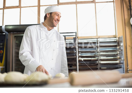 Man in his thirties shaping dough balls on wooden prep table in bakery with rolling pin 133291458