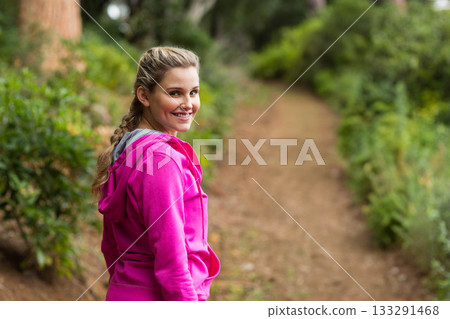 Woman standing on forest dirt trail wearing bright pink hoodie and smiling at camera Woman standing on forest dirt trail wearing bright pink hoodie and smiling at camera 133291468