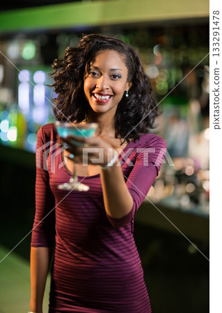 African American woman holding blue martini glass and smiling at bar with illuminated bottles African American woman holding blue martini glass and smiling at bar with illuminated bottles 133291478
