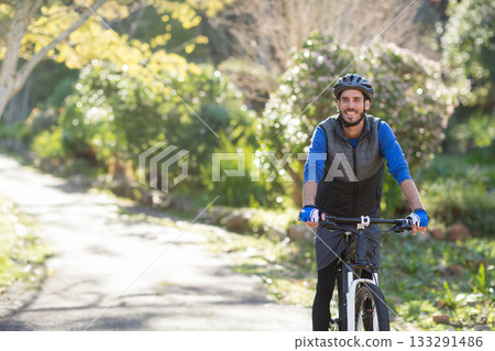 Male cyclist riding mountain bike along sunlit paved park trail with helmet and gloves, copy space 133291486