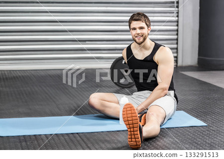 Adult male fitness enthusiast sitting on blue mat in gym with weight plate, water bottle 133291513