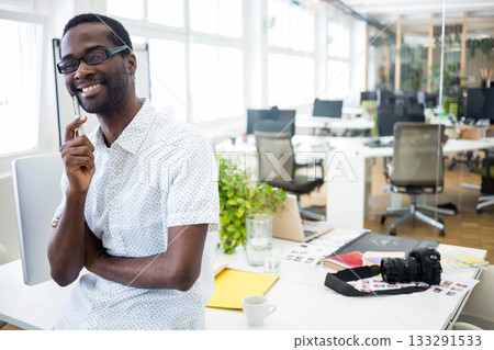 African American man leaning while holding pen at chin in office with DSLR camera, copy space 133291533