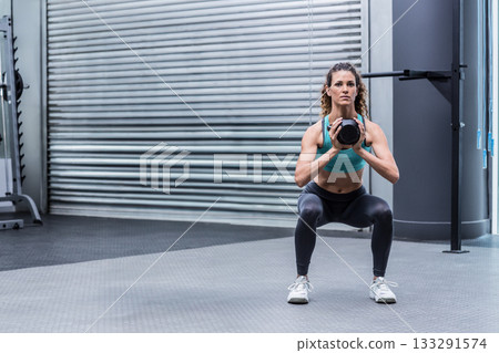 Female athlete wearing sportswear performing weighted squat at gym with kettlebell, copy space Female athlete wearing sportswear performing weighted squat at gym with kettlebell, copy space 133291574