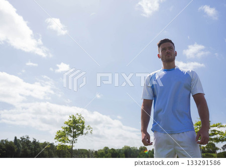 Man standing on sports field wearing athletic jersey and shorts under bright sky, copy space 133291586
