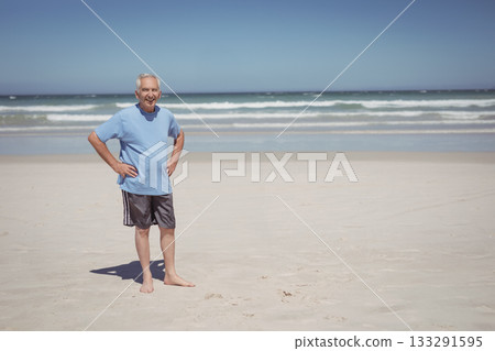 Senior man standing barefoot on sandy beach by gentle ocean waves above horizon line, copy space 133291595